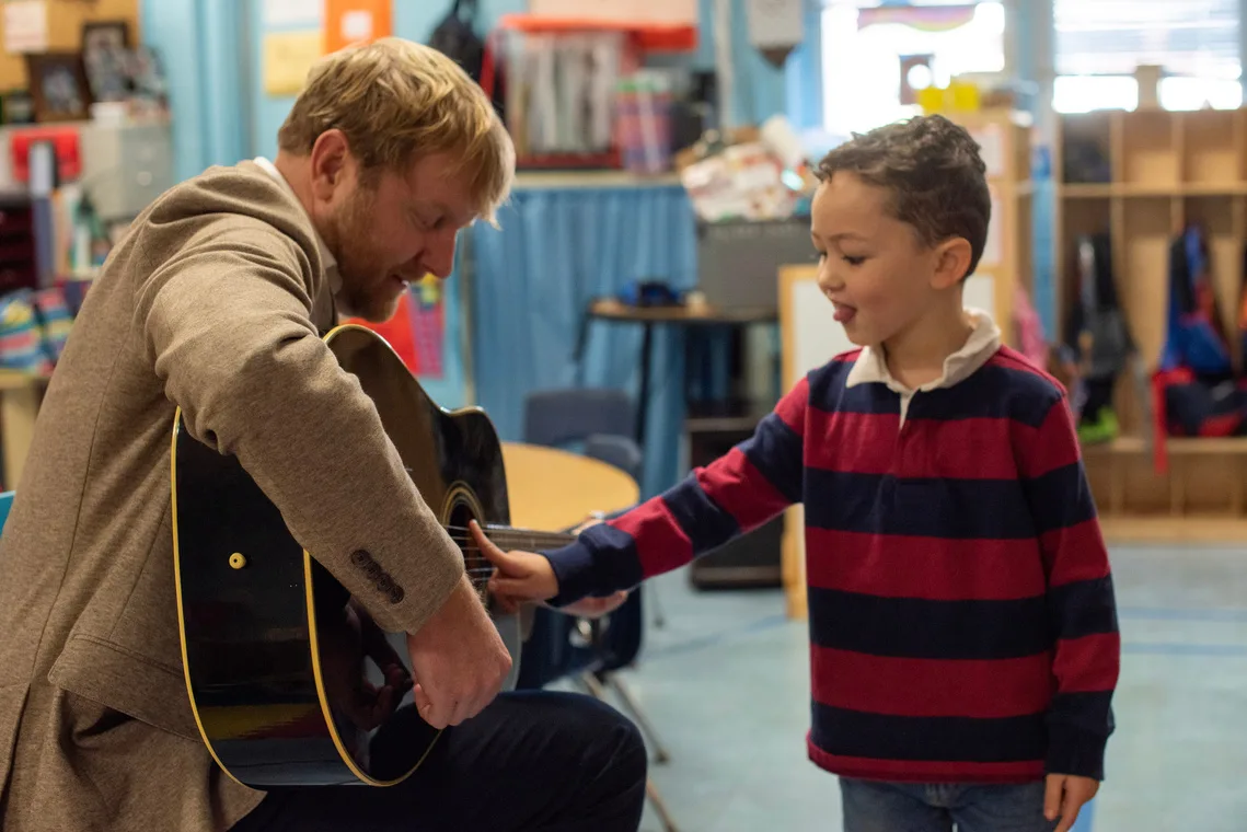 Stephen playing guitar with a young student in a classroom